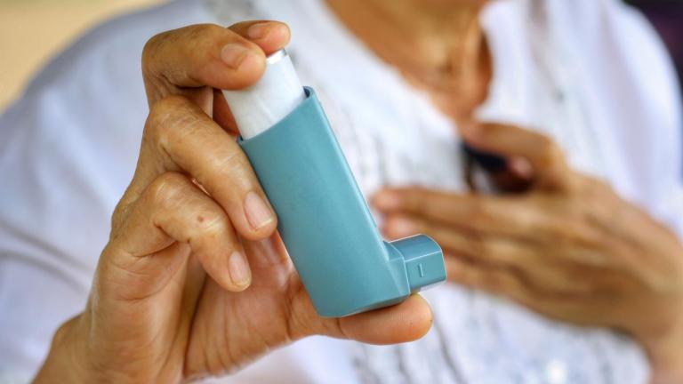 An older woman holds an inhaler