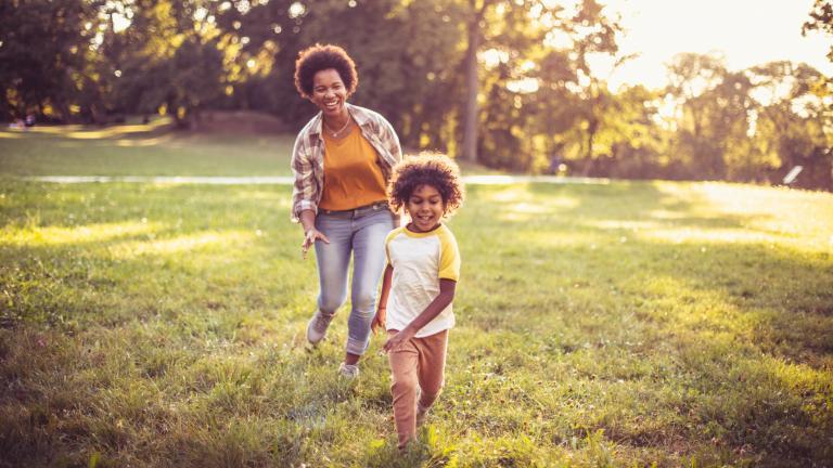 A woman runs after a young child as they laugh playing outside.