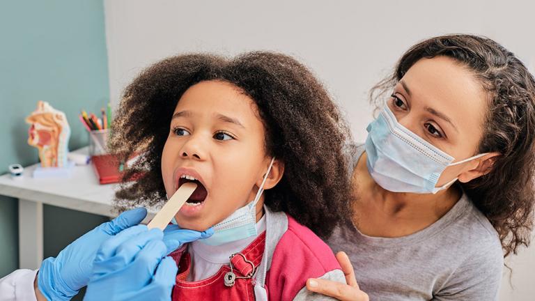 This photo shows a child with her parent during pediatrician appointment. The doctor uses a small tongue depressor to help examine the girl’s throat for signs of disease. Credit: Shutterstock