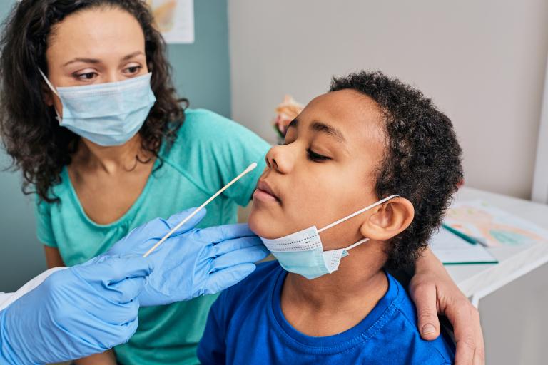 Boy undergoes nasal swab test at doctor's office while mother looks at him. 