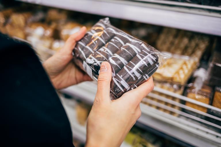 Hands of a young woman hold a pastry as she looks for label of ingredients.