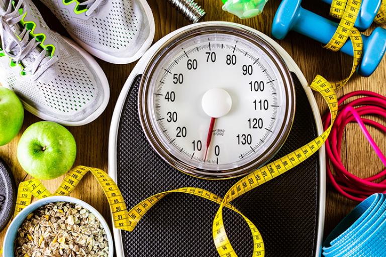 photo of a exercise equipment, bowl of oatmeal and apples, a measuring tape, workout shoes, and a weight scale
