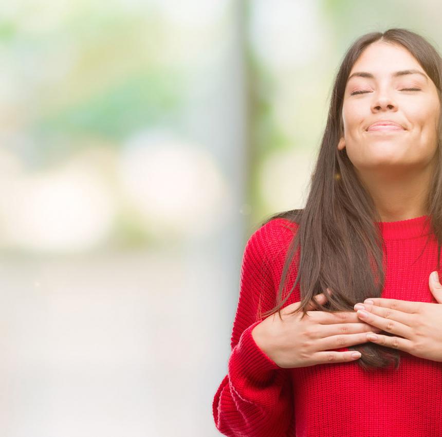 Woman wearing red with her hands touching her heart, smiling