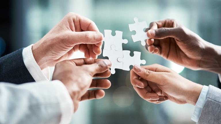 Four hands holding up puzzle pieces together.