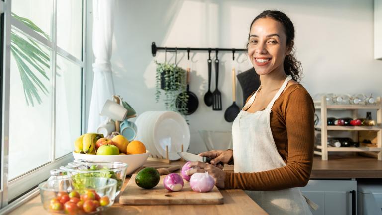 young Latina woman smiling and chopping vegetables in the kitchen 