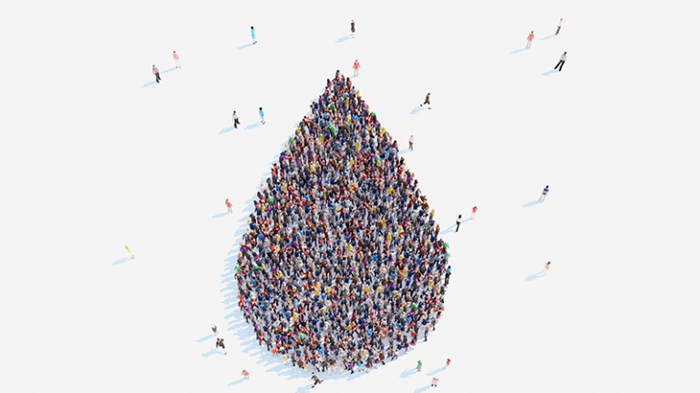 An overhead view of a crowd of people standing closely together to make the shape of a blood drop.