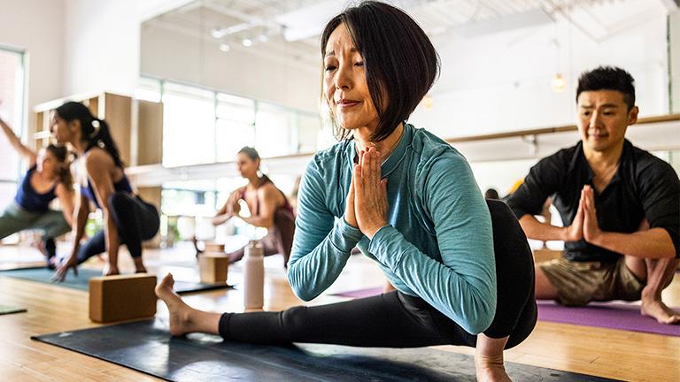 A woman and three other adults are in a yoga class.