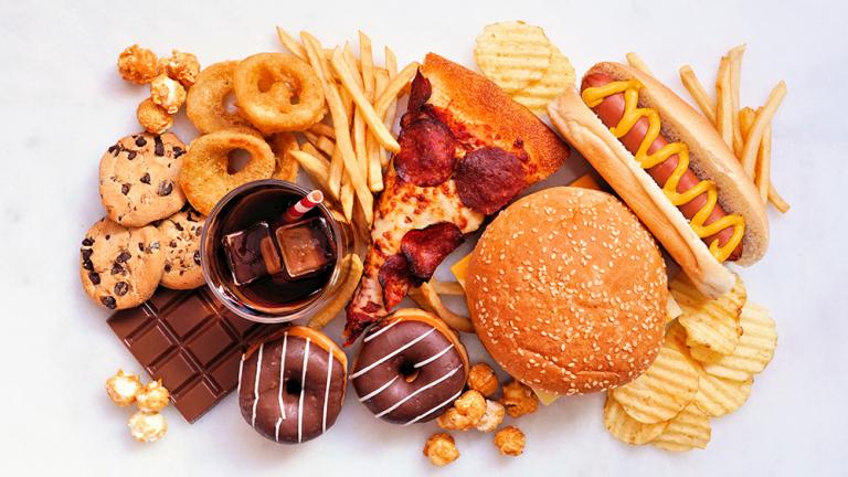 Collection of ultra-processed foods scattered over a white background. Includes hot dog, pizza, soda, fries, sweets, and other foods. Credit: Shutterstock