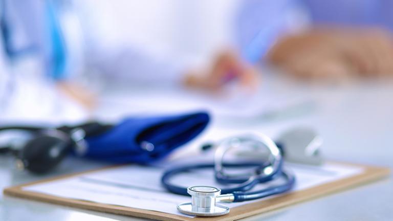 A stethoscope and blood pressure cuff are shown on top of a clipboard.