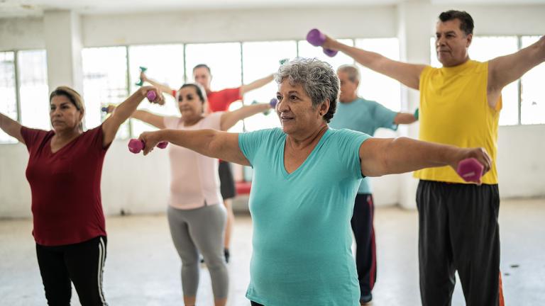 a group of Hispanic adults exercise with handheld weights in a class