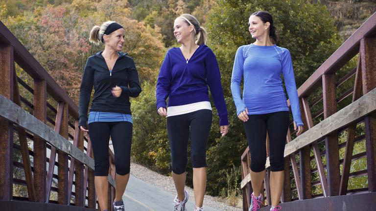 three women in exercise clothes walk over a bridge