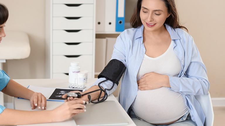 A pregnant woman is at a doctor’s office getting her blood pressure checked by a healthcare provider.