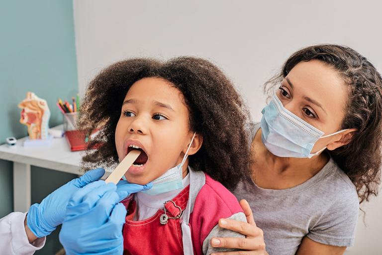 This photo shows a child with her parent during pediatrician appointment. The doctor uses a small tongue depressor to help examine the girl’s throat for signs of disease. Credit: Shutterstock