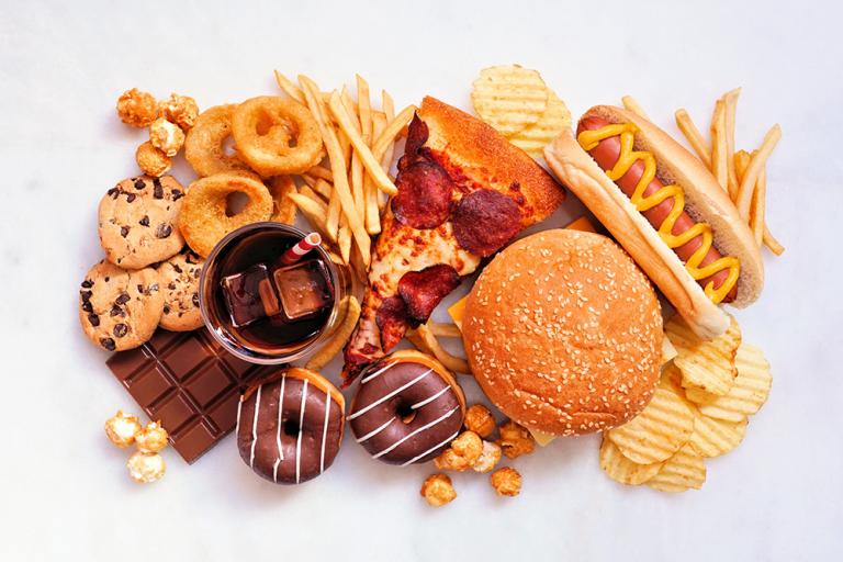 Collection of ultra-processed foods scattered over a white background. Includes hot dog, pizza, soda, fries, sweets, and other foods. Credit: Shutterstock