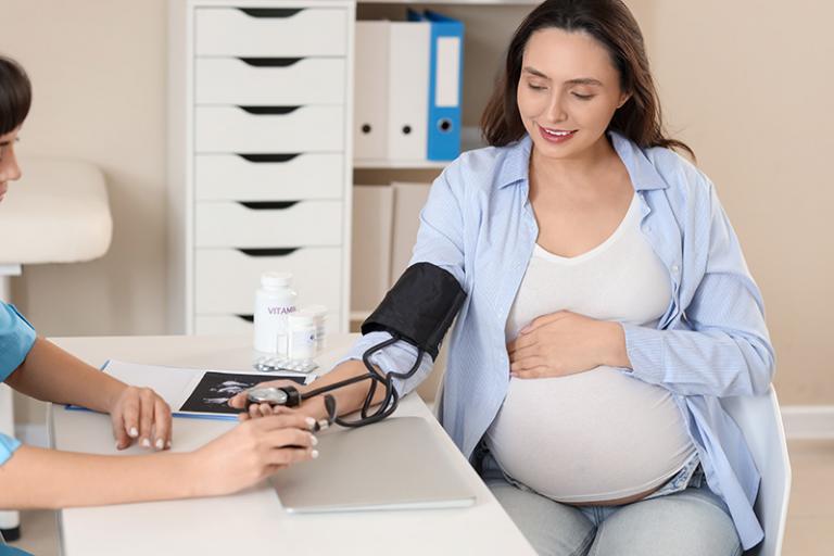 A pregnant woman is at a doctor’s office getting her blood pressure checked by a healthcare provider.