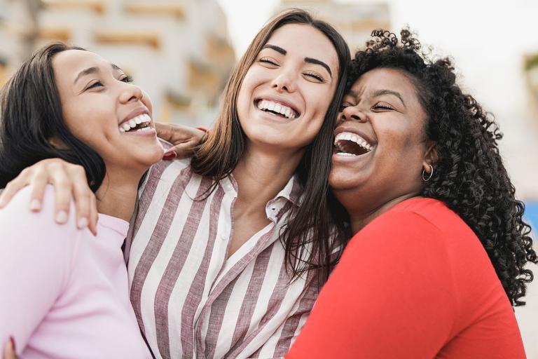 three latino young women laughing and hugging